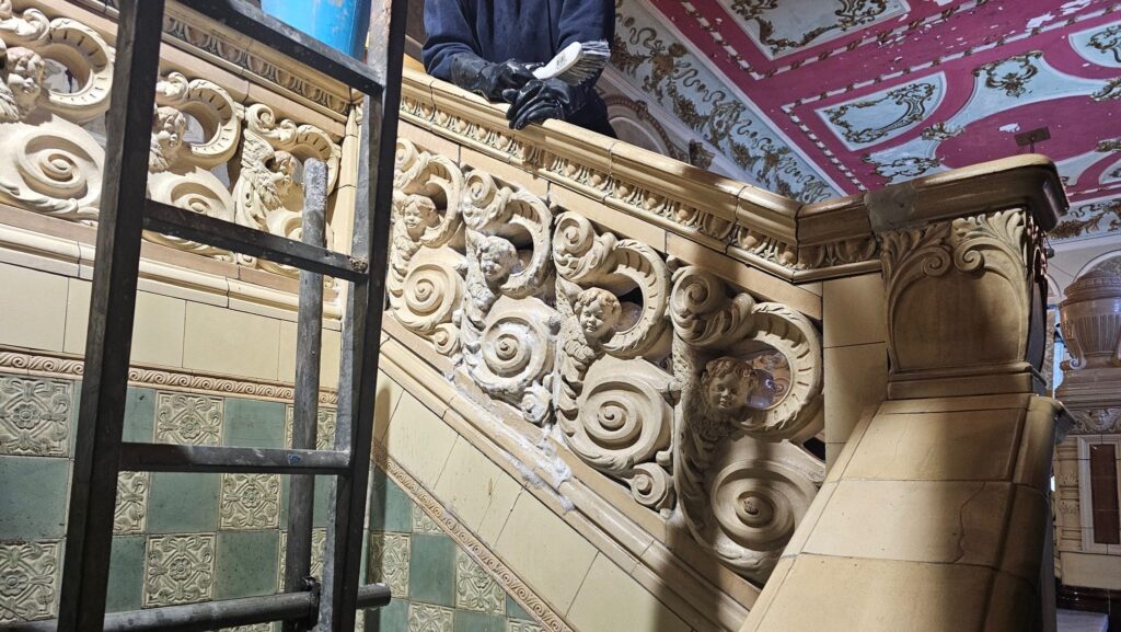 A person in rubber gloves cleaning the ceramic decoration on a staircase in Morecambe Winter Gardens